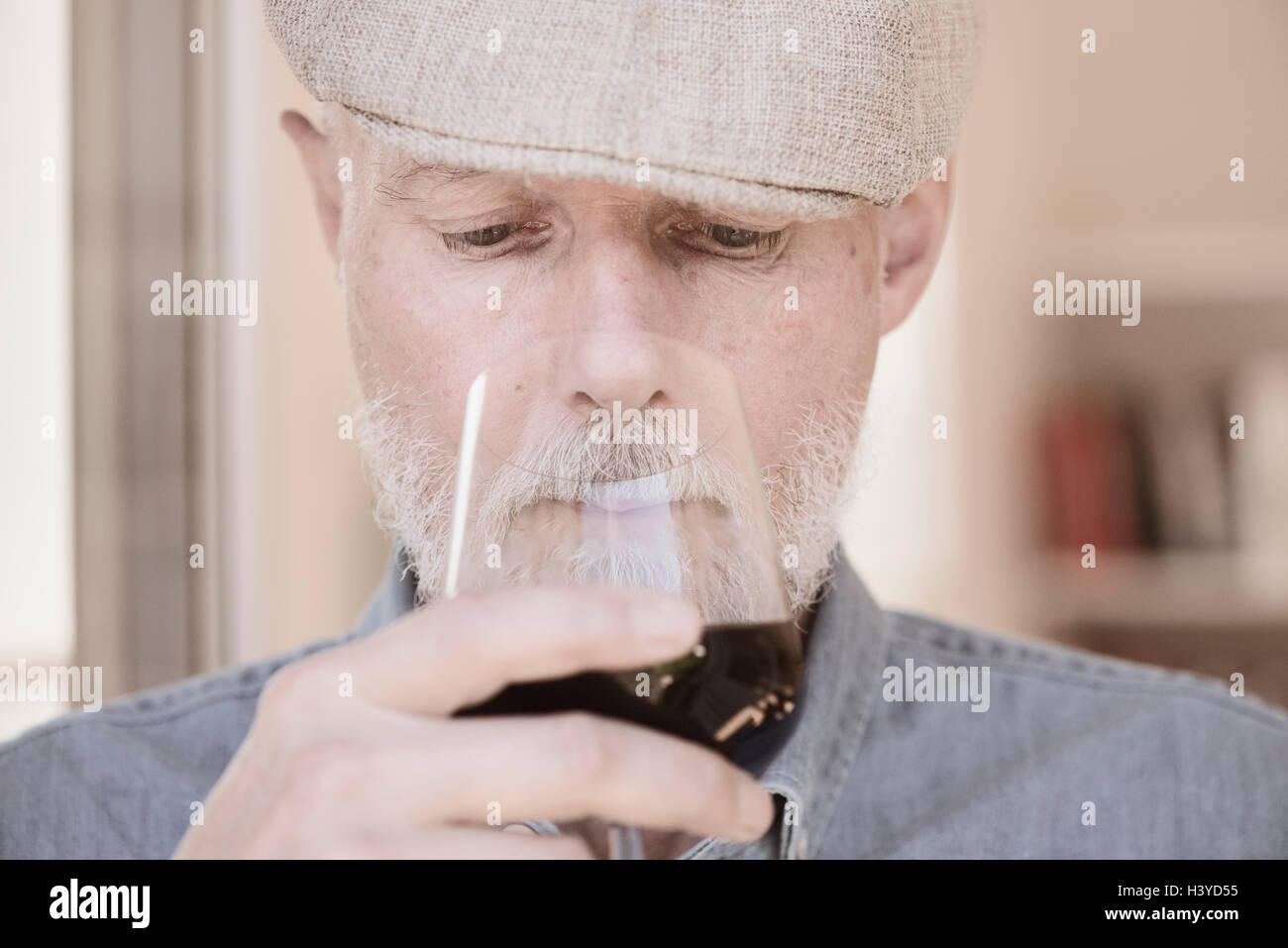 Old man in cap holding wineglass. Smelling the red wine with serious expression. Stock Photo