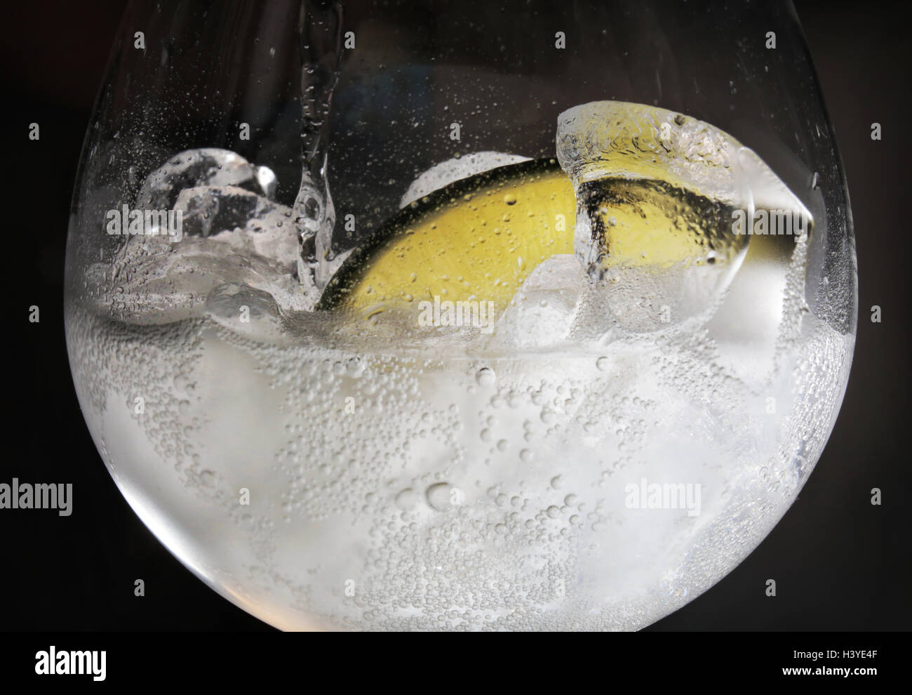 A gin and tonic being poured in a bar with a slice of lime and ice