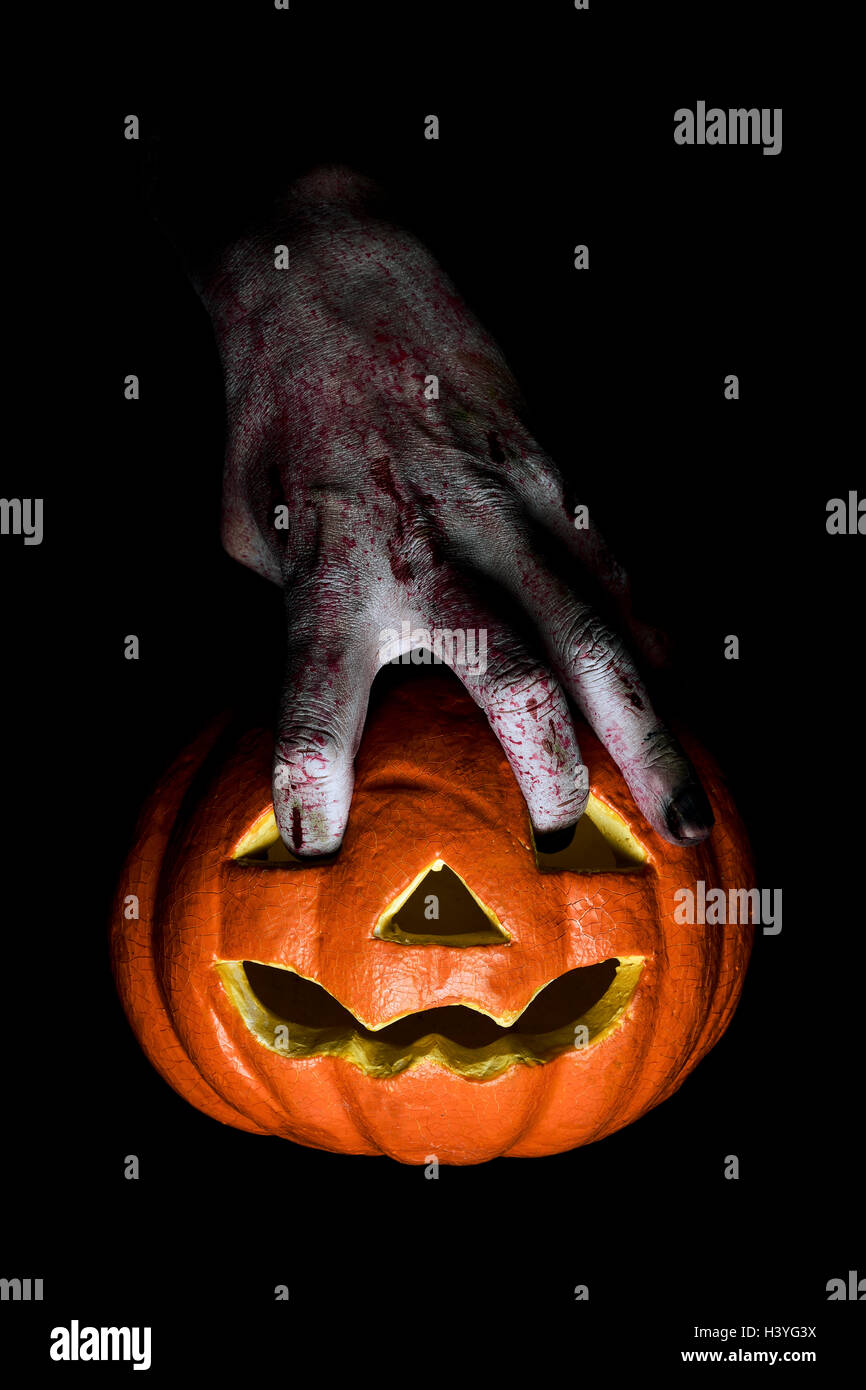 closeup of the scary hand of an undead man putting his fingers in the holes of a carved pumpkin Stock Photo