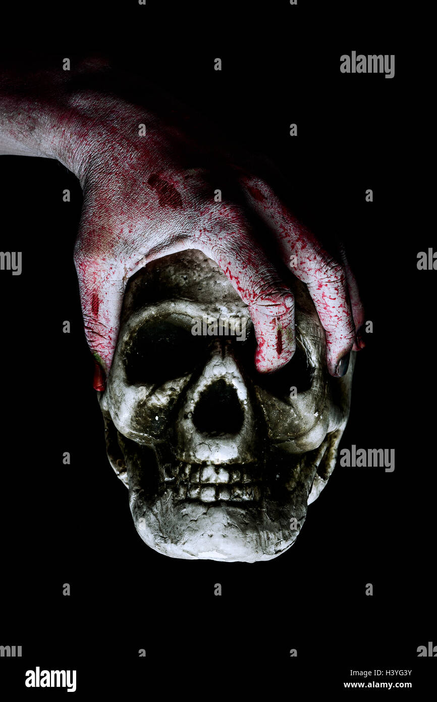 closeup of the scary hand of an undead man holding a skull against a black background Stock Photo