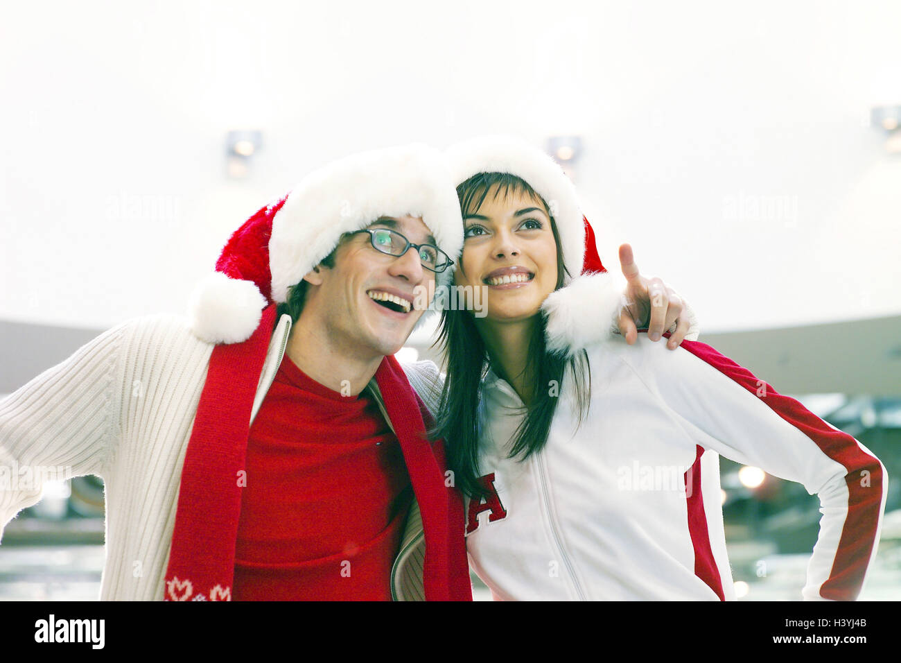 Shopping centre, couple, young, happy, Santa's hats, point, half portrait, yule tide, Christmas period, department store, purchasing, shopping, shop, Christmas shopping, enthusiasm, cheerfulness, joy, observing, together, embrace, affection, happy, caps, glasses, wearers glasses Stock Photo