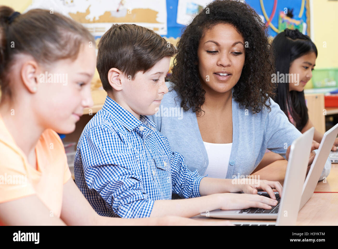 Teacher Helping Male Elementary Pupil In Computer Class Stock Photo