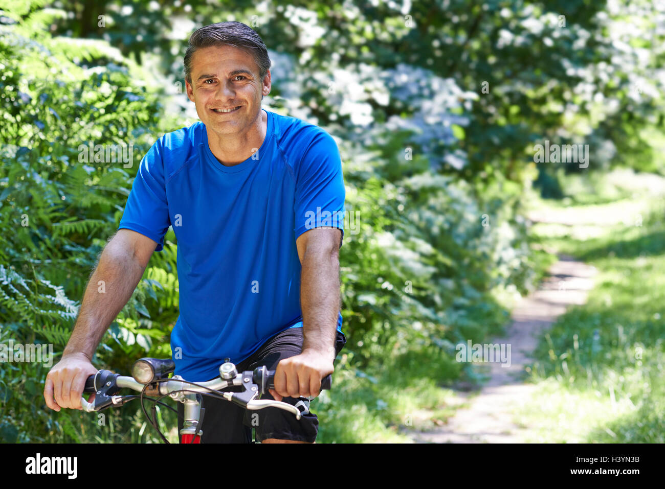 Mature Man Cycling Along Path In Countryside Stock Photo