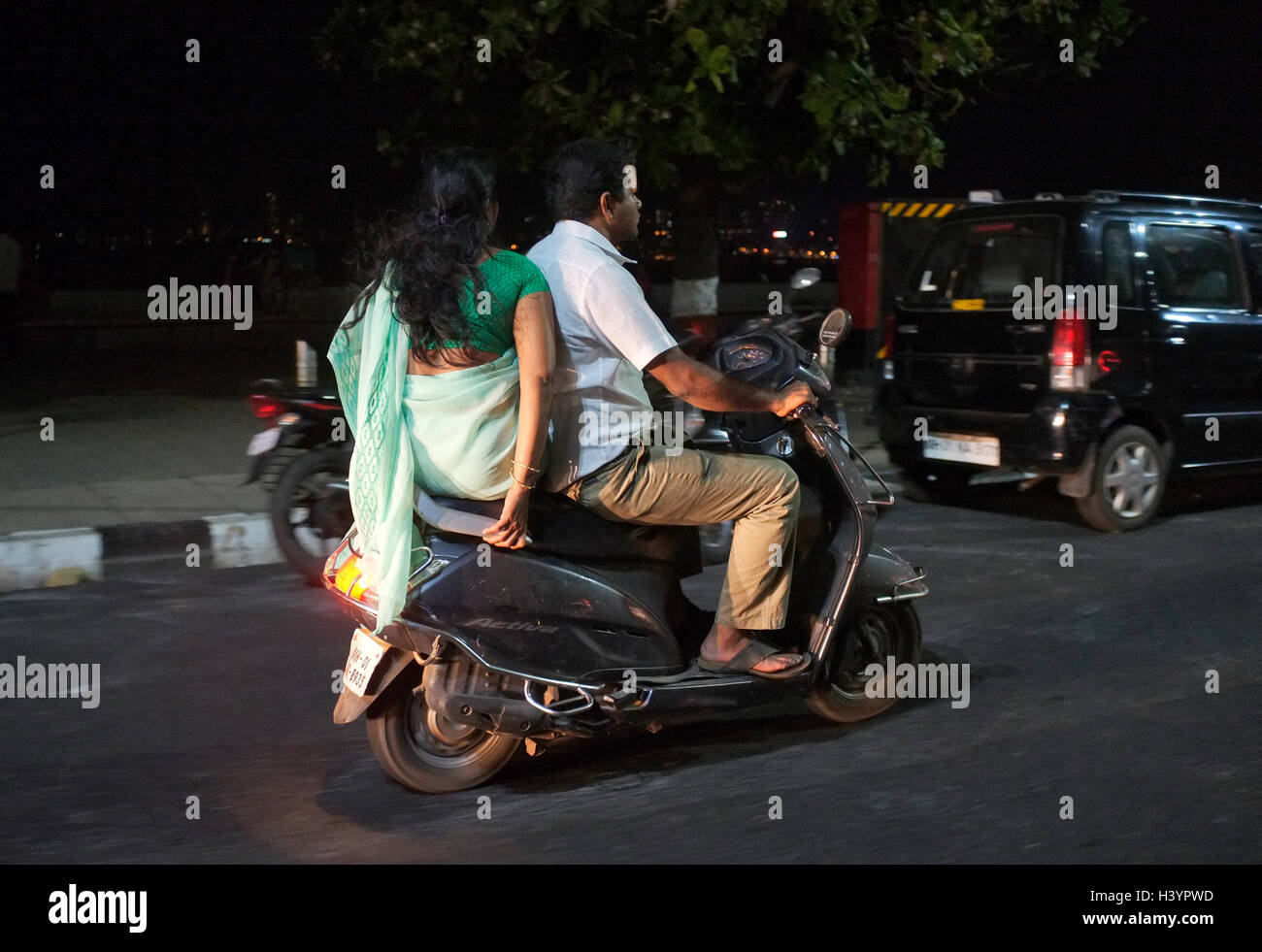 a women in saree rides side saddle in back of motor scooter. Street