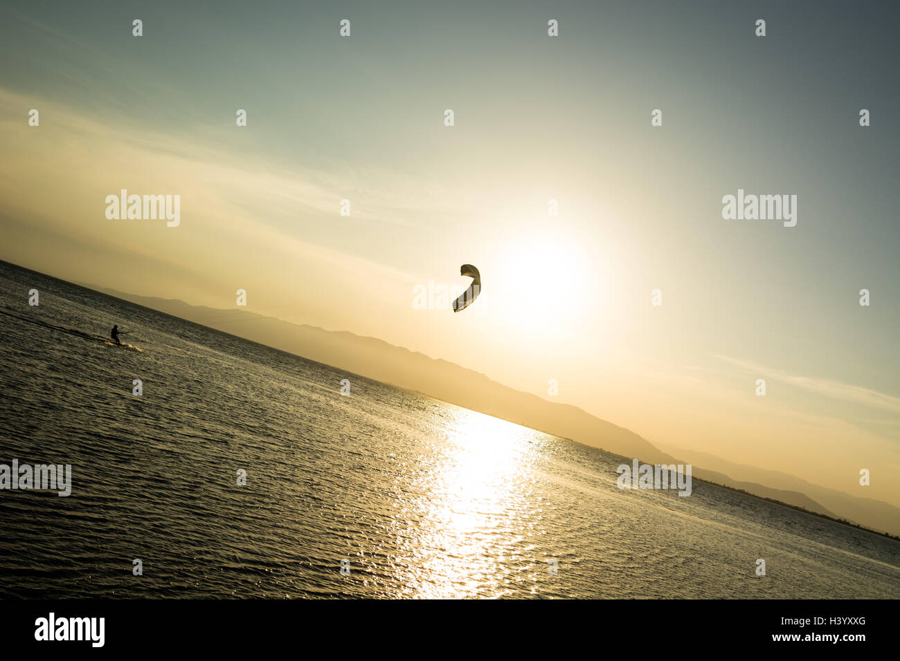 A person doing kitesurf in a calmed bay at sunset. Stock Photo