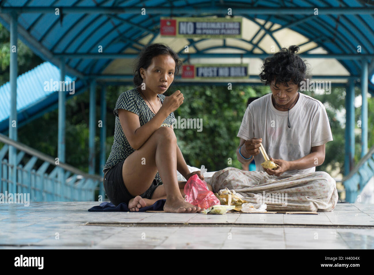 Homeless man & woman sit eating food within an elevated skywalk in Cebu City,Philippines Stock Photo