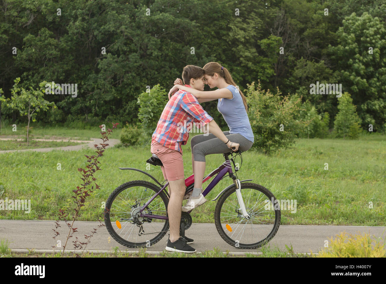 Romantic couple sitting face to face on bicycle against trees at park Stock Photo