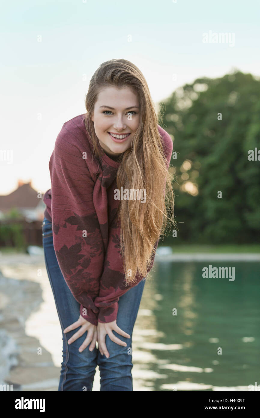 Portrait of cheerful young woman with long hair standing by lake Stock Photo