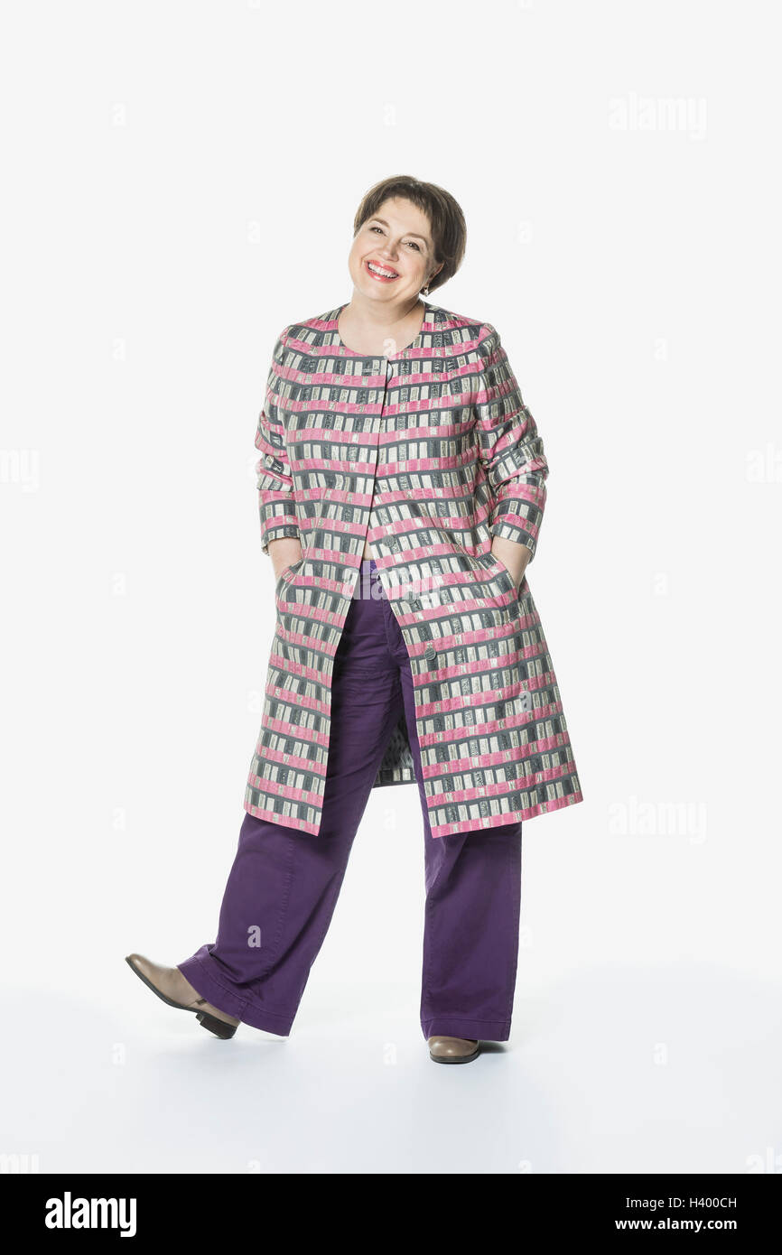 Portrait of smiling woman standing with hands in pockets against white ...