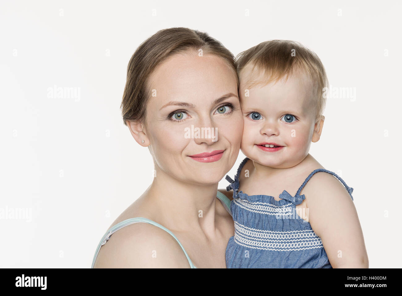 Portrait of smiling mother carrying cute girl against white background Stock Photo