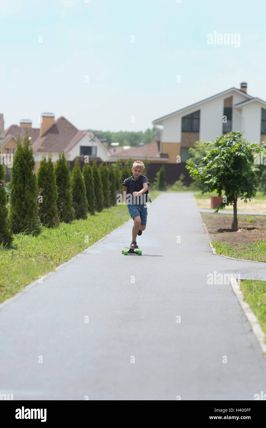 Boy skateboarding on road amidst trees against houses in town Stock Photo