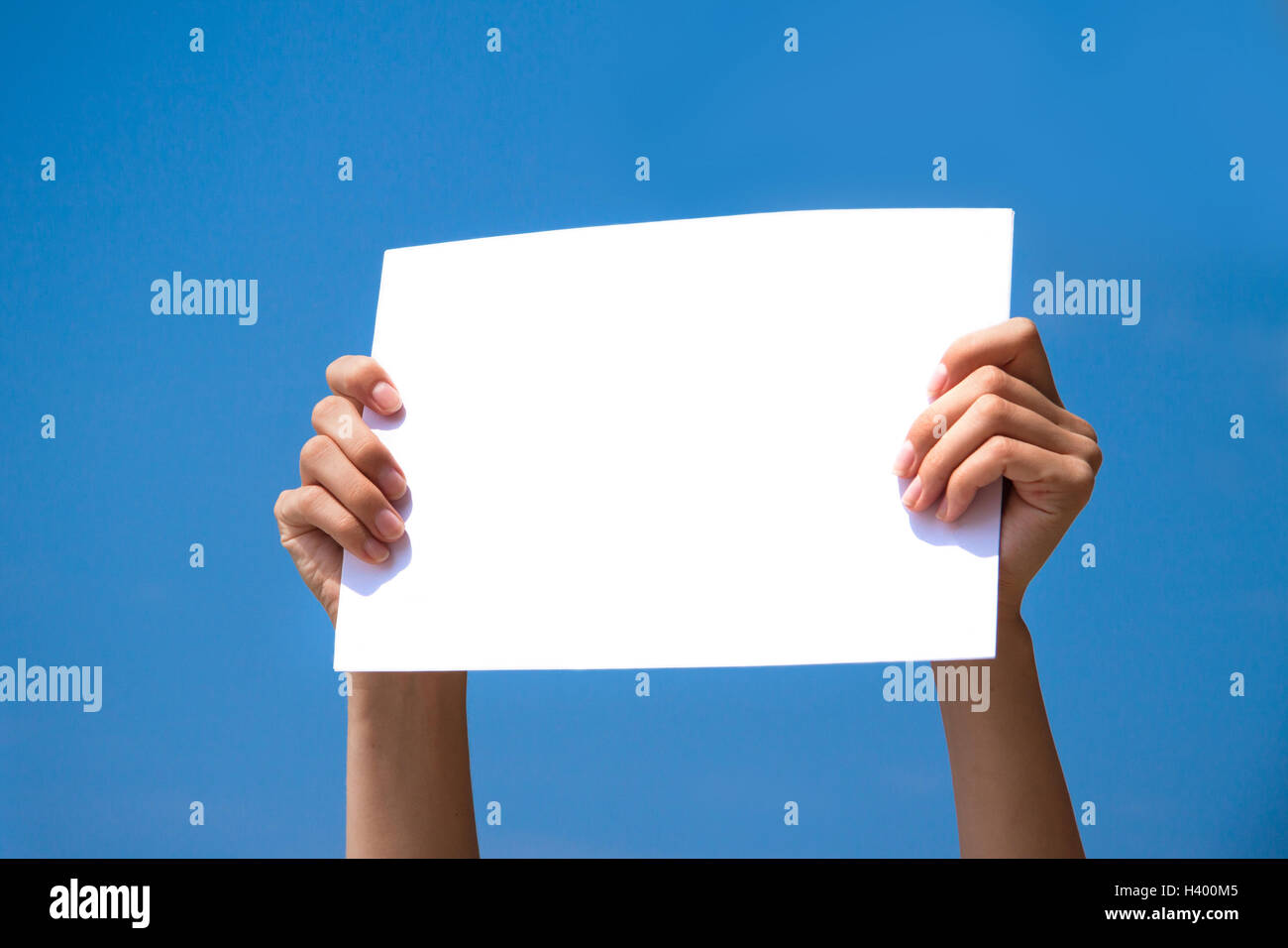 Person holding a blank page in its hands with blue sky background Stock Photo