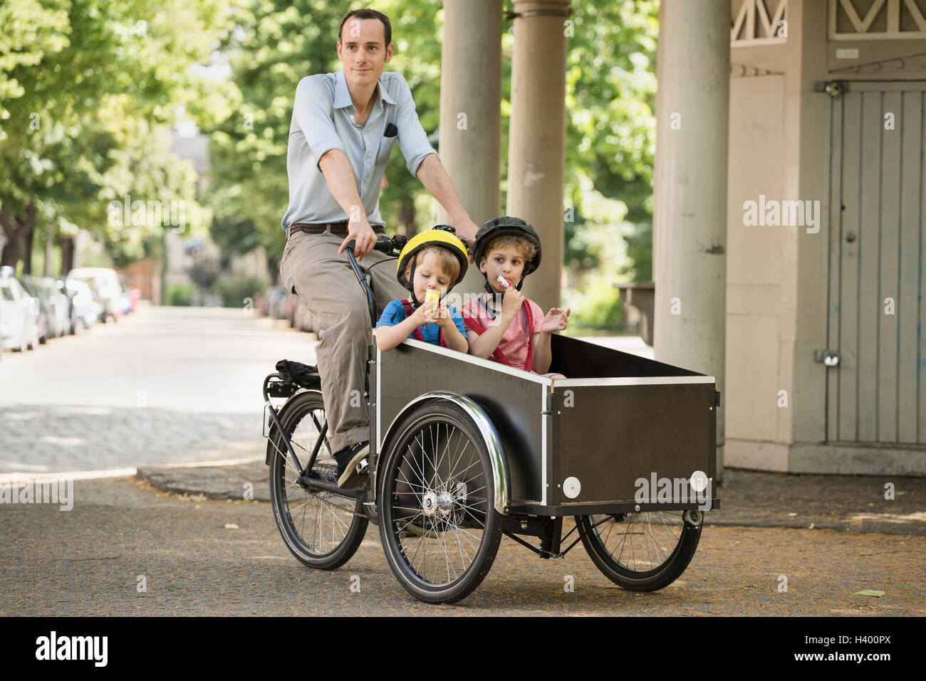 Father with boys riding bicycle with cart on street Stock Photo