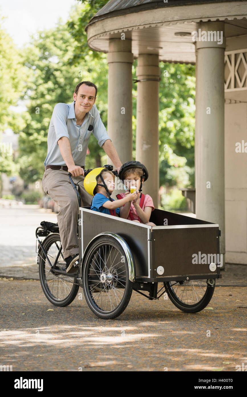 Smiling father riding bicycle while boys sitting in cart on street Stock Photo