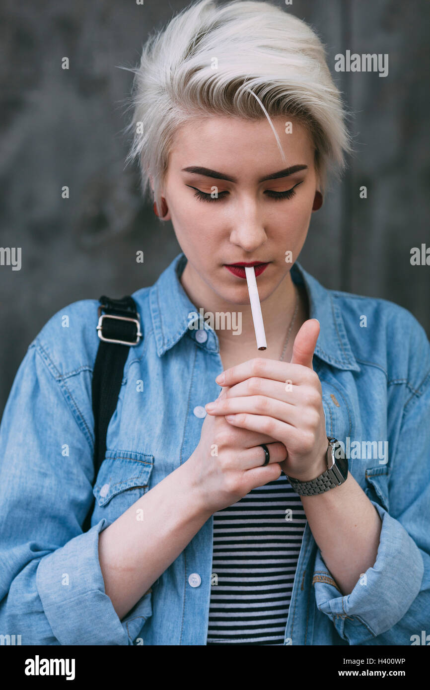 Young fashionable woman smoking cigarette while standing outdoors Stock Photo