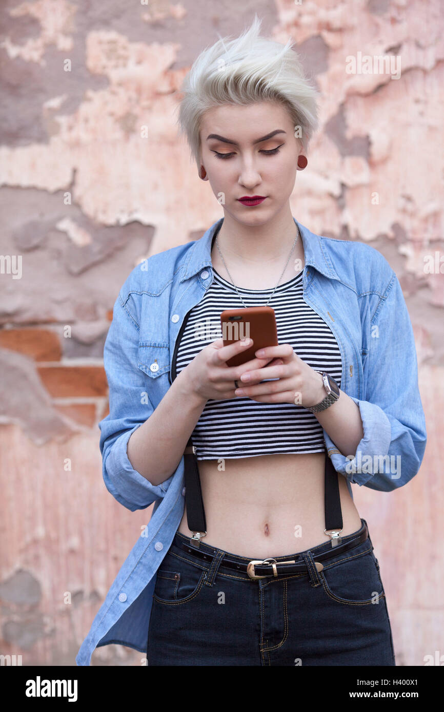 Beautiful woman using phone while standing against old wall Stock Photo