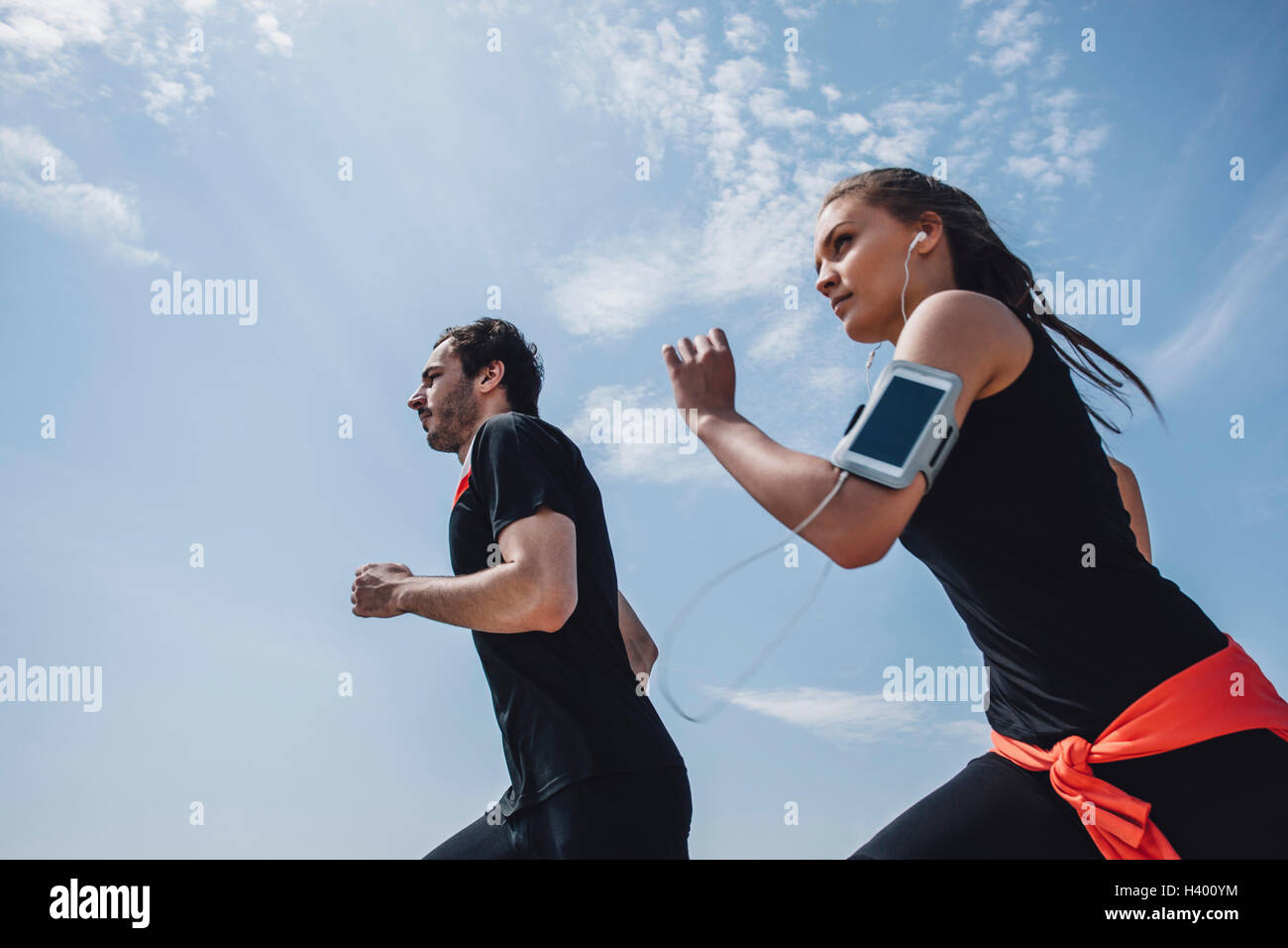 Low angle view of young man and woman jogging against sky Stock Photo