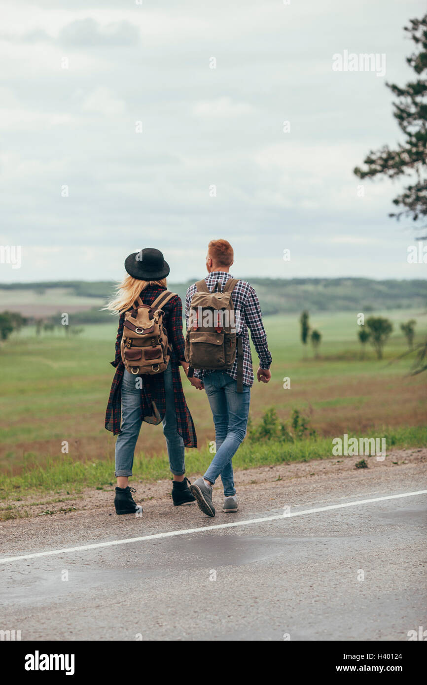Couple walking on roadside by field against sky Stock Photo