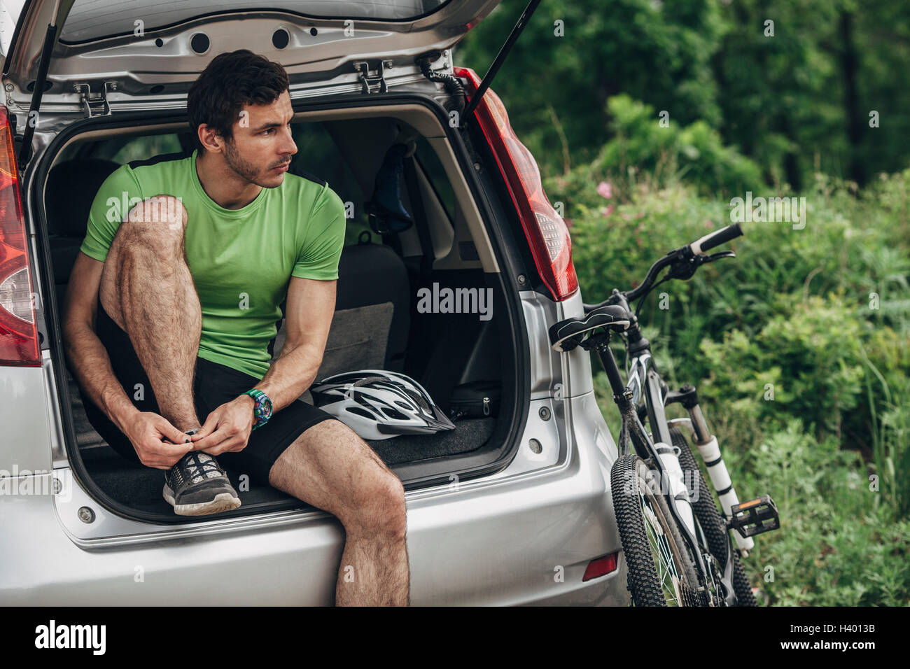 Man tying shoelace while sitting in car trunk Stock Photo