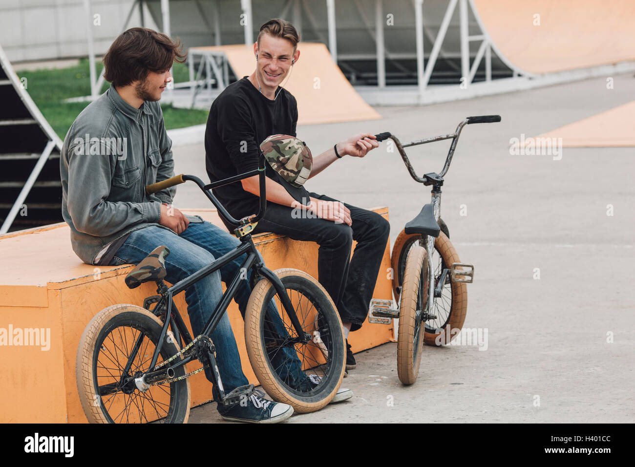 Cheerful friends resting on seat with bicycles at skateboard park Stock Photo
