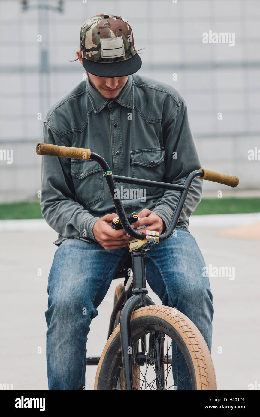 Teenager using phone while sitting on bicycle at skateboard park Stock Photo