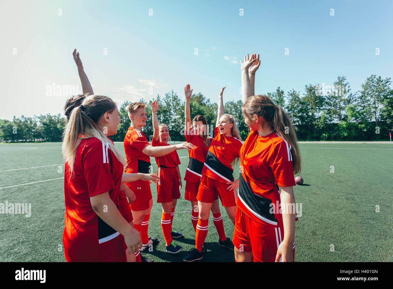 Excited soccer players with hands raised standing on field Stock Photo