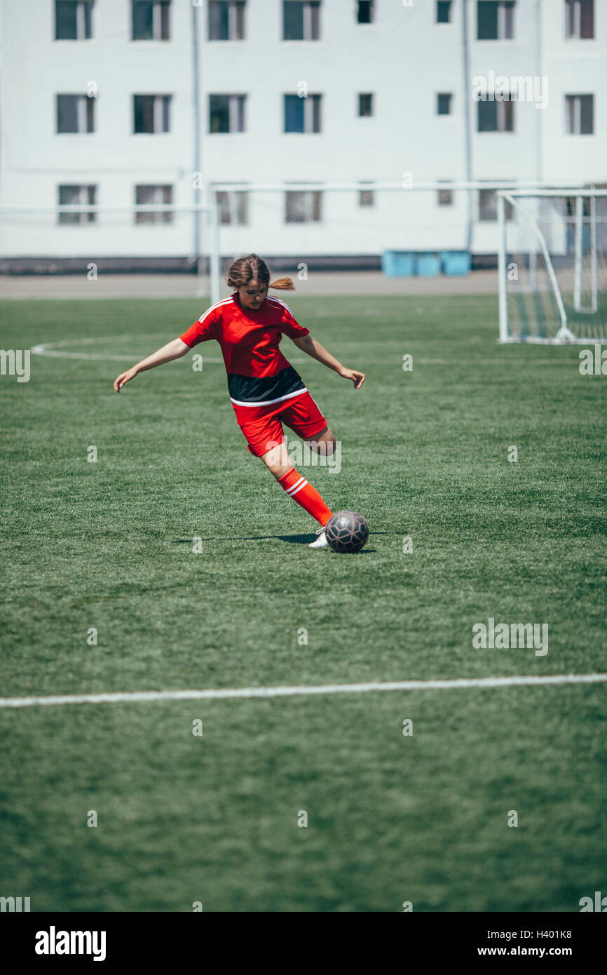 Determined teenager kicking ball on soccer field Stock Photo