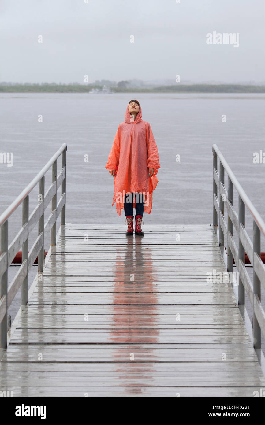 Woman wearing raincoat standing on jetty during rainy season Stock