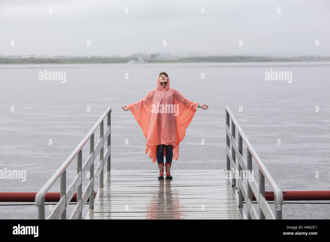 Woman wearing raincoat enjoying rainy season while standing on jetty Stock Photo