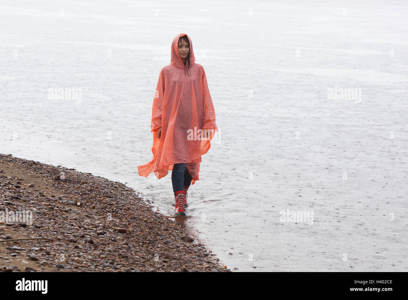 Woman wearing raincoat walking at lakeshore during rainy season Stock