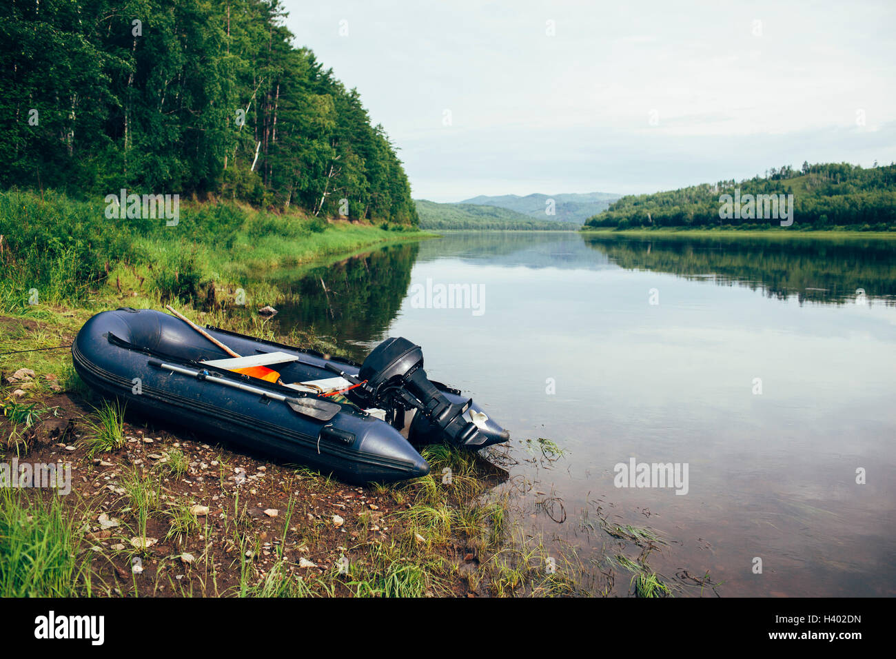 Inflatable motorboat moored at riverbank in forest against sky Stock Photo