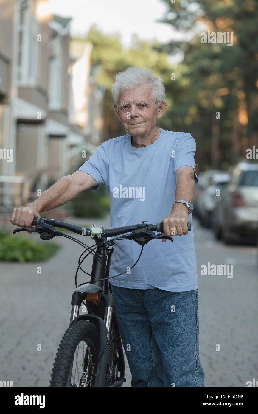 Portrait of senior adult standing with bicycle on city street Stock Photo