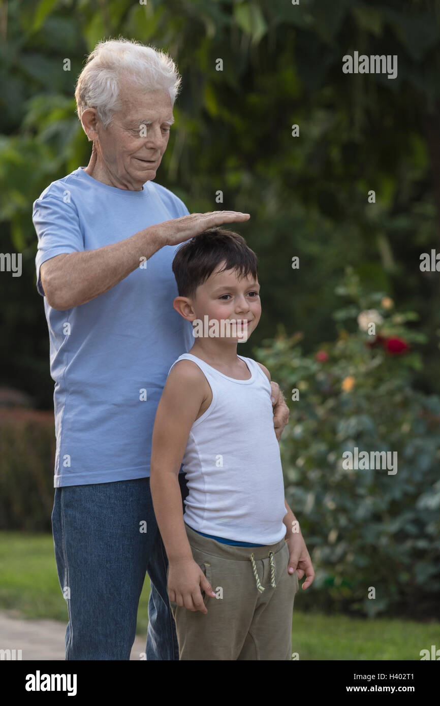 Smiling grandfather measuring grandson's height while standing at park Stock Photo
