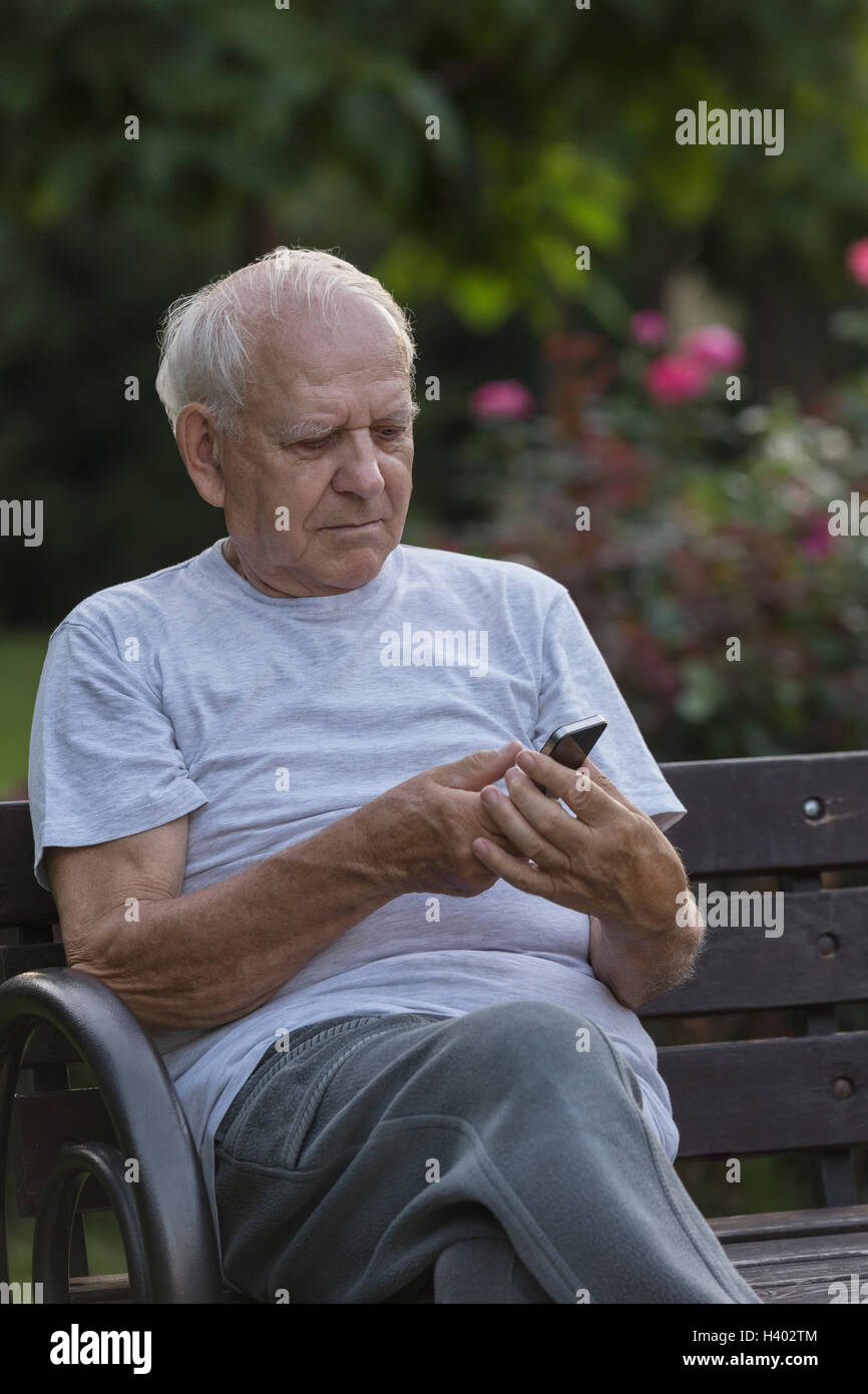 Smiling man using smart phone while sitting on park bench Stock Photo
