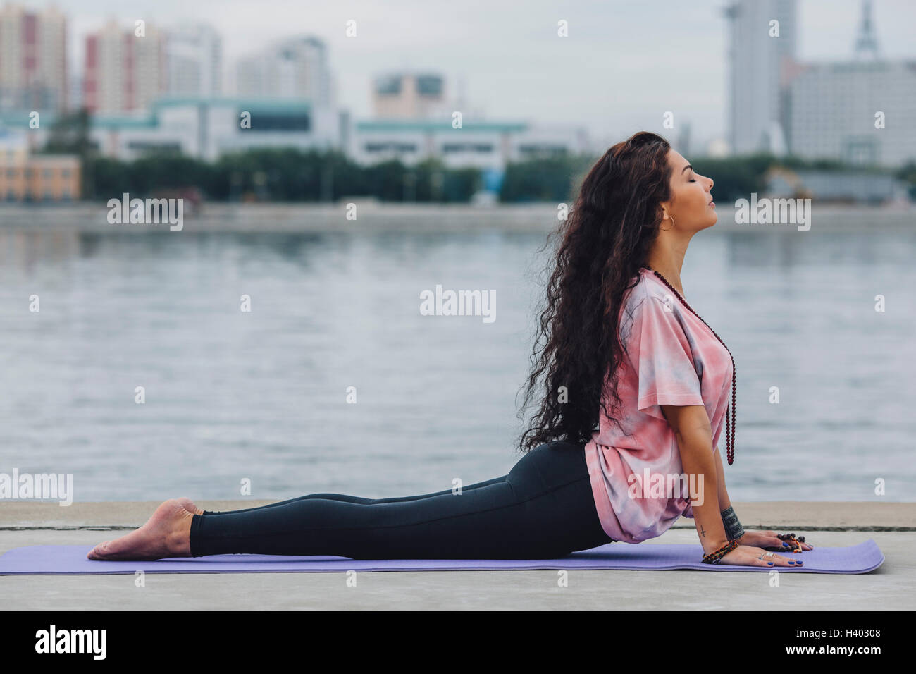 Side view of woman practicing yoga in cobra pose by river at city Stock Photo