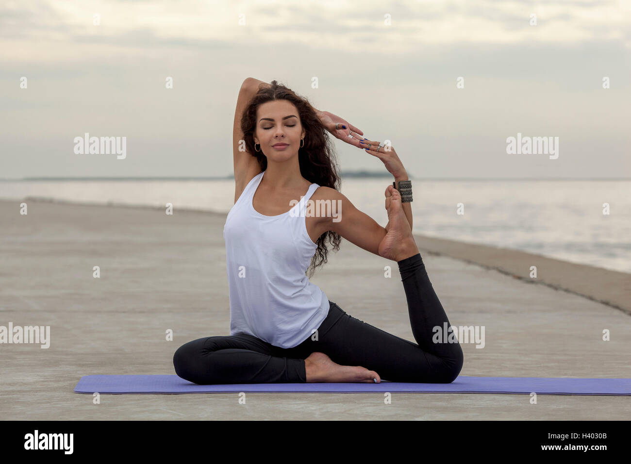 Beautiful woman practicing yoga in mermaid pose at beach Stock Photo