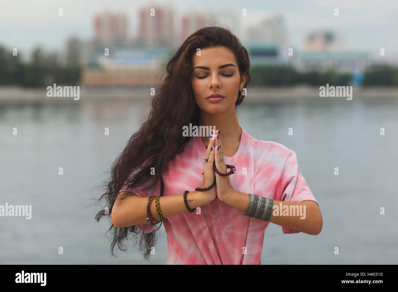 Woman with closed eyes meditating in prayer position against river Stock Photo