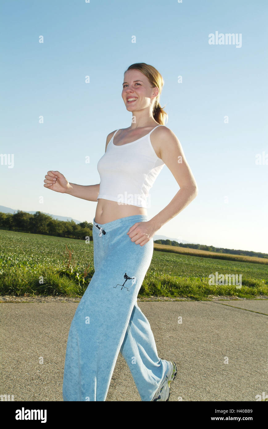 Country lane, woman, young, jog, smile side view, fields, way, young persons, 19 years, happily, smile, leisure time, hobby, sport, sportily, sportswoman, running, jogging, motion, activity, fitness, stress reduction, equaliser, enjoy, evening light, back Stock Photo