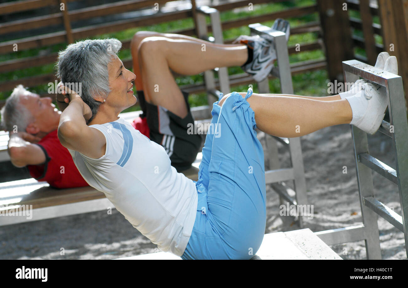 Trimm-dich-Pfad, senior citizens, training device, lie, Sit-ups, at the side, 50-60 years, couple, sportily, sport, activity, gymnastics, gymnastics exercises, gymnastics practise, health, fitness, training, musculature, strengthening, stomach muscles, abdominal muscle training, abdominal musculature, rationalisation, consolidation, practise, together, leisure time, hobby, activity Stock Photo