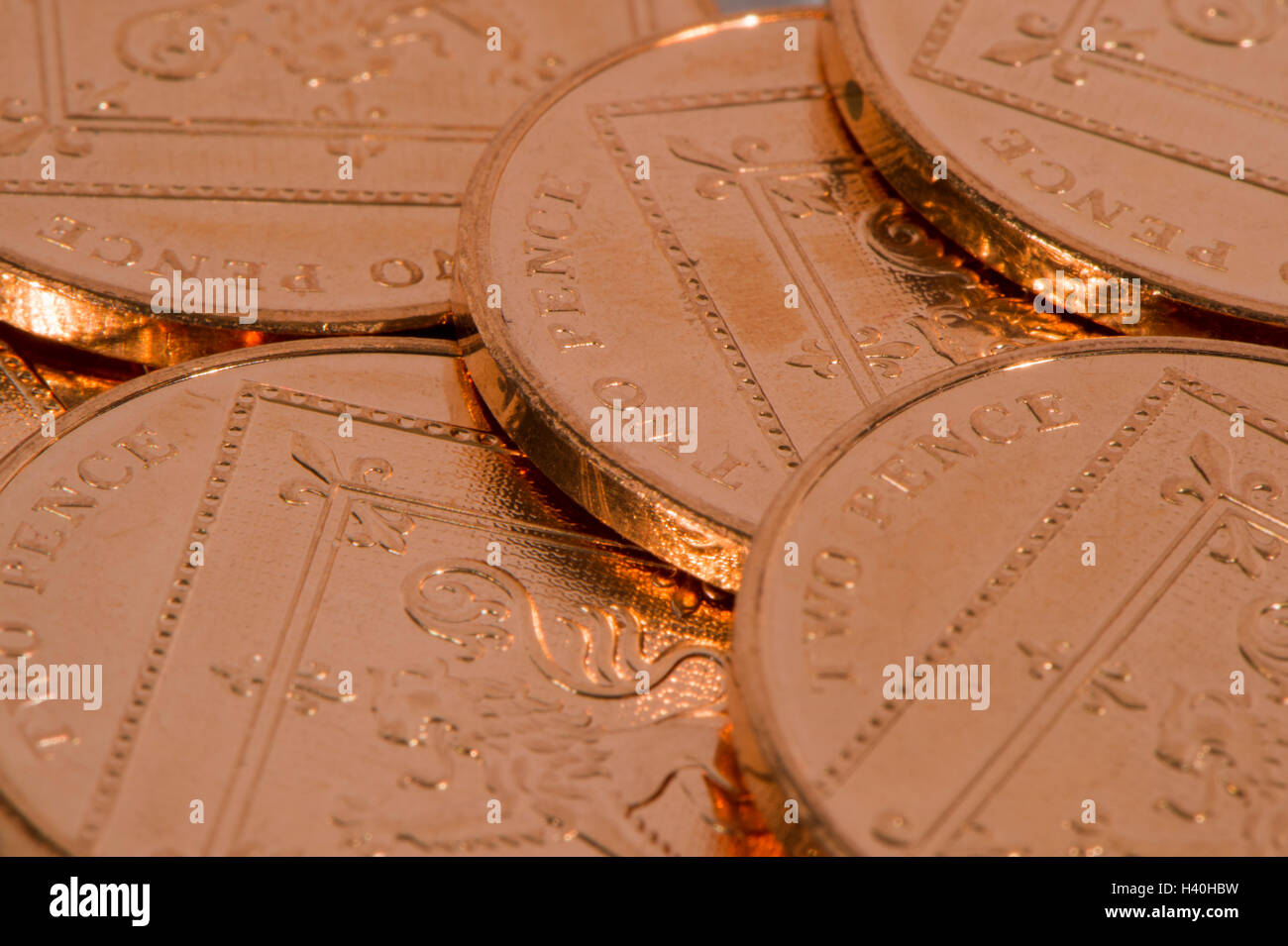 Laid flat and overlapping, 5 shiny, copper, two pence coins, tails up - loose-change and UK money with little value. Stock Photo