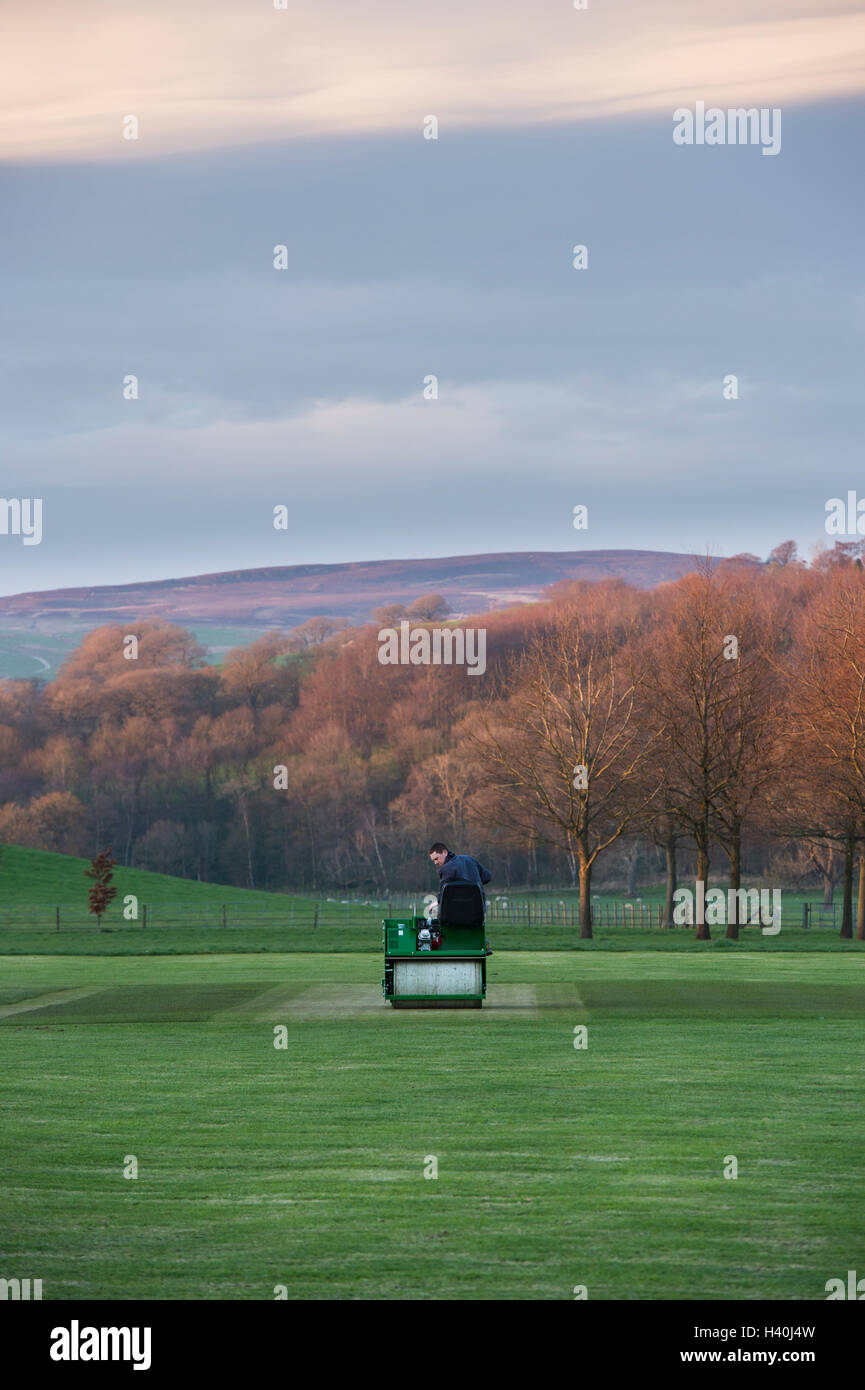 Man driving a ride-on roller, preparing the wicket of a village cricket pitch - Bolton Abbey Cricket Club, Yorkshire Dales. Stock Photo