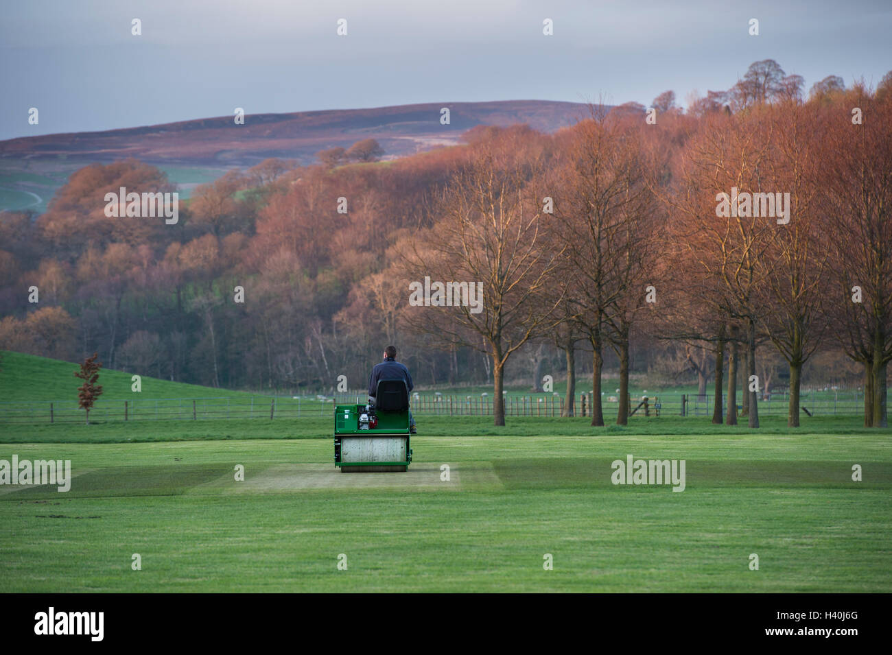 Man driving a ride-on roller, preparing the wicket of a village cricket pitch - Bolton Abbey Cricket Club, Yorkshire Dales. Stock Photo