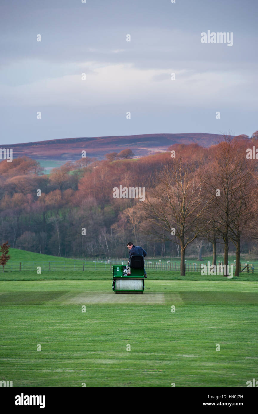 Man driving a ride-on roller, preparing the wicket of a village cricket pitch - Bolton Abbey Cricket Club, Yorkshire Dales. Stock Photo