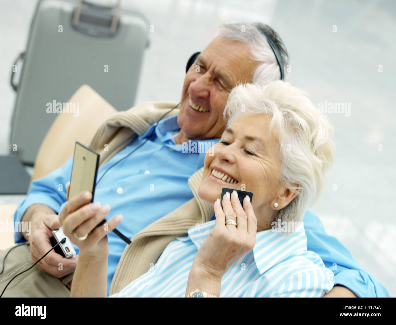 Airport, attendant zone, senior pair,  sits, waits, embrace, happy   Airport hall, chairs, bank, seats, pair, seniors, passengers, passengers, tourists, wait, man, headphones, music, music audition, woman, hand mirrors, hears make up, face powders are too Stock Photo