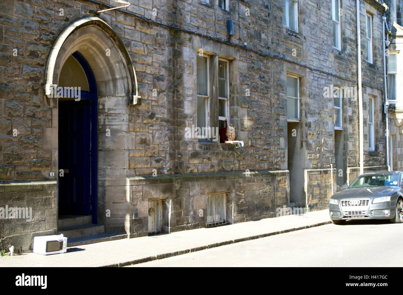 University student reads book whilst hanging out the window in St Andrews Stock Photo