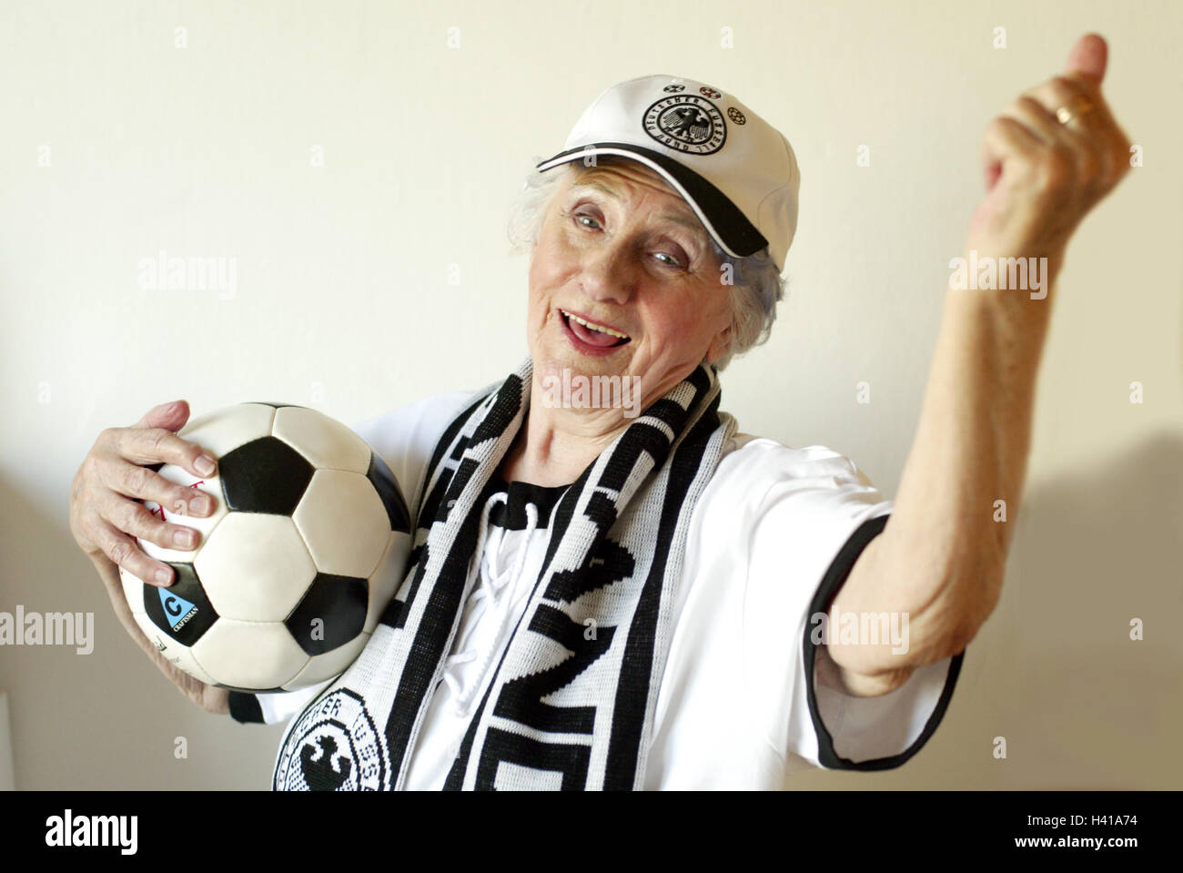 Senior, football fan, happily, gesture, cheering, ball, portrait, sport, football match, spectator, senior, pensioner, woman, old, agile, actively, young remaining, football follower, fan, follower, hobby, keen on sport, confidently, is convincing, motivates certainly about victory, happily, enthusiastically, contently, hope, optimism, confidence, laugh, rejoice, joy, enthusiasm, passion, fist, victory, tuning positively, German Football Association, German Football Association-fan article, fan article in an old-fashioned way, outfit, football, scarf, cap, cap, headgear, national pride, in Stock Photo