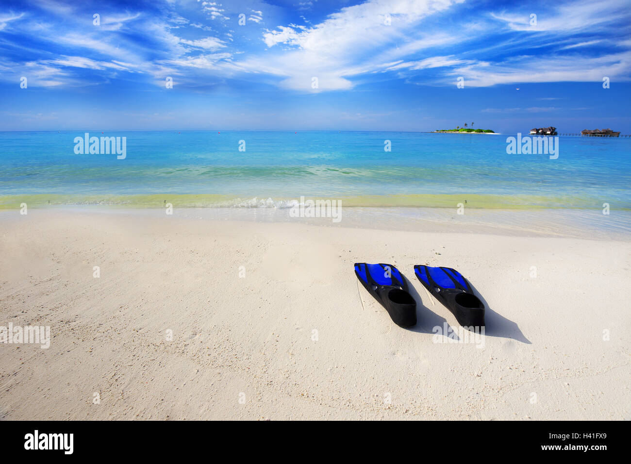 Tropical island with sandy beach with overwater bungalows, turquoise clear water and snorkeling equipment Stock Photo