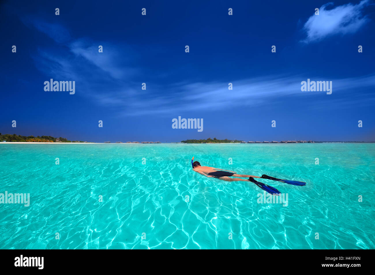 Young man snorkling in tropical lagoon with over water bungalows Stock Photo