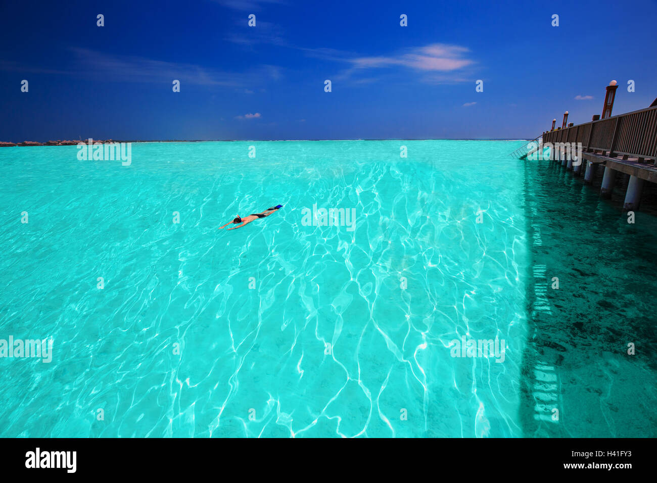 Young man snorkling in tropical lagoon with over water bungalows Stock Photo