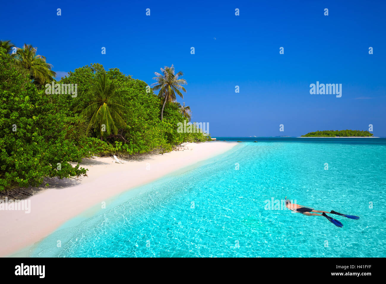 Young man snorkling in tropical island with sandy beach, palm trees and turquoise clear water Stock Photo